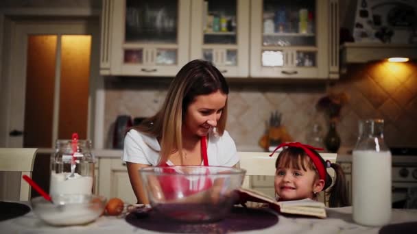 Mom and daughter in the kitchen in a red apron read the recipe cake in a notebook. — Stock Video