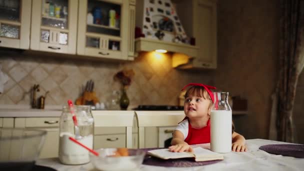 Mamma och dotter i köket i ett rött förkläde Läs recept kakan i en anteckningsbok. — Stockvideo