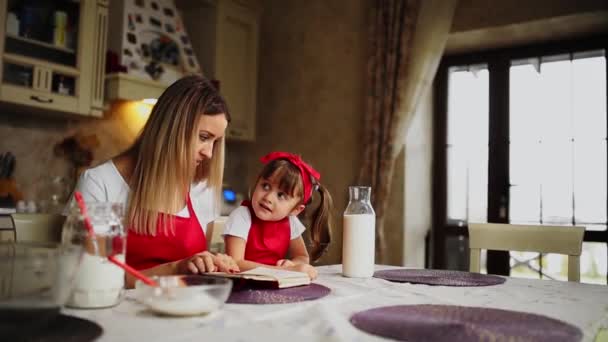 Mutter und Tochter in der Küche in roter Schürze lesen das Rezept in einem Notizbuch. — Stockvideo