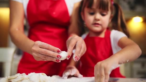 Gelukkige familie in de keuken moeder en dochter in de keuken spelen met bloem plezier te hebben en de balletjes in de keuken in de dezelfde rode schorten schimmel. stedicam — Stockvideo