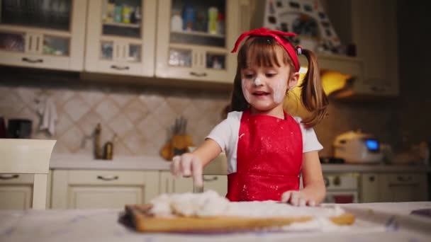 Das kleine Mädchen in der Küche, das mit Teig und Mehl spielt, klatscht und lacht. Herumalbern in der Küche. — Stockvideo