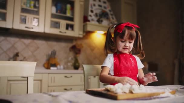 Das kleine Mädchen in der Küche, das mit Teig und Mehl spielt, klatscht und lacht. Herumalbern in der Küche. — Stockvideo