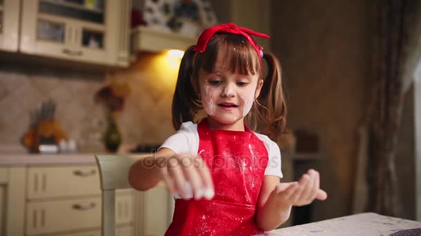 Das kleine Mädchen in der Küche, das mit Teig und Mehl spielt, klatscht und lacht. Herumalbern in der Küche. — Stockvideo