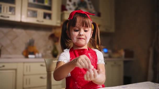 Маленькая девочка на кухне играет с тестом и мукой, хлопает и смеется. Глупости на кухне. . — стоковое видео