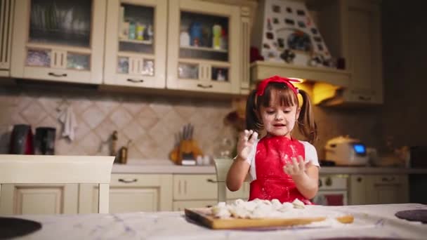 Het kleine meisje in de keuken spelen met deeg en meel, klapt en lacht. Gek rond in de keuken. — Stockvideo