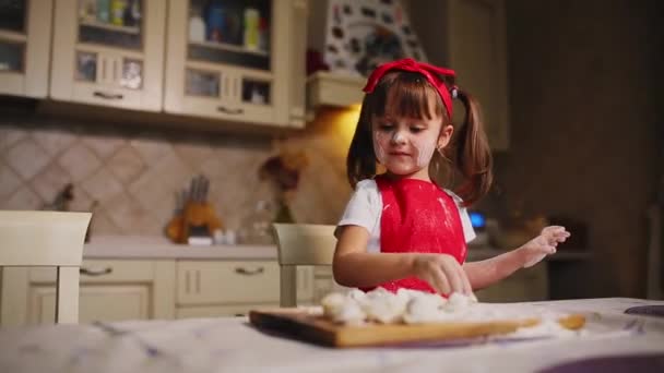 A kis lány a konyhában, játszani a tésztát, és liszttel, tapsol és nevet. Bolondozás körül a konyhában. — Stock videók
