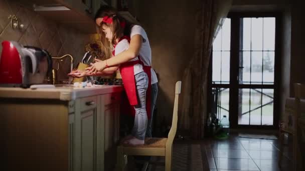 Mãe ajuda a lavar as mãos de sua filha na cozinha depois de cozinhar o jantar . — Vídeo de Stock