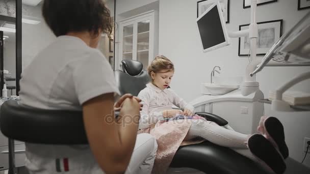 Childrens tandarts voert overleg met het kleine meisje in mijn kantoor. De arts praat met een meisje dat toekomstige behandeling bespreken. — Stockvideo