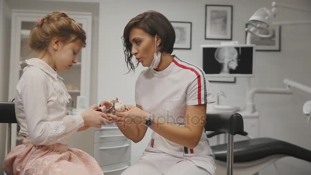 The dentist conducts a consultation a little girl showing how to brush teeth with a toothbrush using a denture. Close-up. Girl learns to brush teeth with braces. — Stock Video