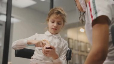 Diş hekimi nasıl bir takma diş kullanarak bir diş fırçası ile diş fırçalama gösteren küçük bir kız bir Danışma yürütmektedir. Yakın çekim. Diş telleri ile diş fırçalama kız öğrenir.