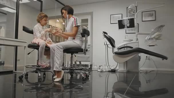 牙医办公室的牙科医生在一个小女孩的 x 光头的背景下学习刷牙后安装大括号。牙医进行牙齿清洁咨询. — 图库视频影像