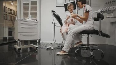 Küçük bir kız diş telleri yükledikten sonra diş fırçalamayı öğrenme x-ray başkanı arka plan üzerinde diş hekimleri office ortodontist. Diş hekimi diş Temizleme için bir Danışma yürütmektedir.