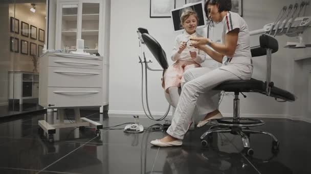 В кабинете стоматолога ортодонт на фоне рентгеновской головы маленькой девочки учится чистить зубы после установки брекетов. Стоматолог проводит консультации по чистке зубов . — стоковое видео