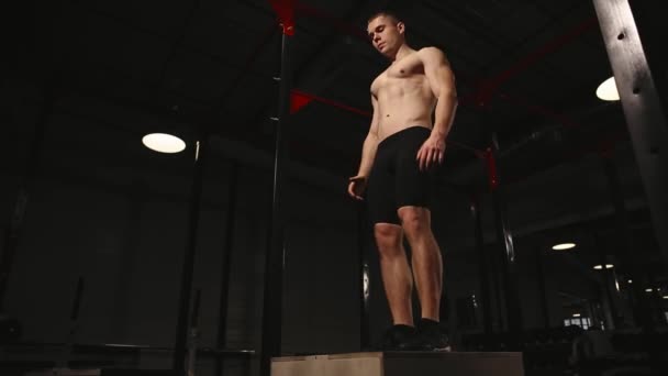 Muscular man without a shirt performs vertical jumps on a wooden box. Aerobic exercise. — Stock Video