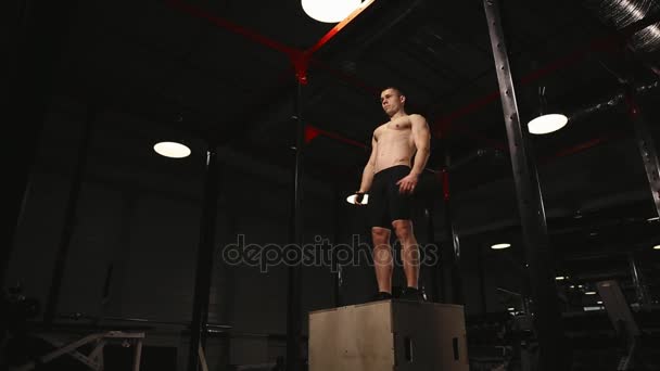 Ein muskulöser Mann ohne Hemd macht vertikale Sprünge auf einer Holzkiste. aerobe Übungen. — Stockvideo