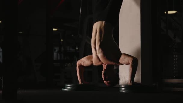 Muscular man standing on hands in the gym by the wall performs push-UPS. — Stock Video