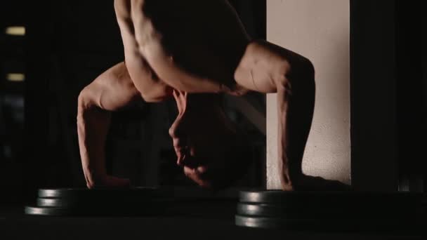 Muscular man standing on hands in the gym by the wall performs push-UPS. — Stock Video