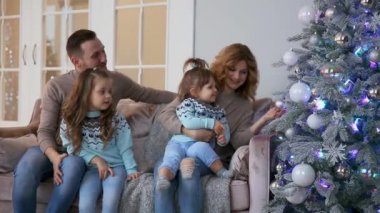 Mutlu aile Noel, anne, baba ve iki küçük kız evde Noel ağacı yakınındaki kanepede oturan hediyeler açmak için.
