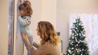 Küçük bir kız kışın pencere pervazına duruyor ve geçen arabaların pencereden bakar.