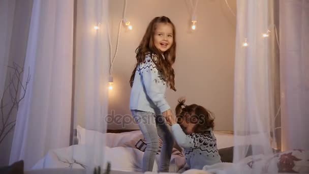 Twee zussen met Kerstmis, springen op het bed in truien, fun, lachen en knuffel. — Stockvideo