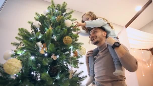 Flickan sitter på pappa på halsen och de dekorera julgranen. — Stockvideo