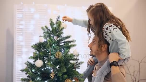 Κορίτσι που κάθεται στο μπαμπά στο λαιμό και που στολίζουν το χριστουγεννιάτικο δέντρο. — Αρχείο Βίντεο