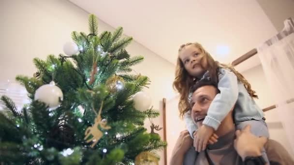 Dívka sedí na tatínka na krku a ozdobit vánoční stromeček. — Stock video
