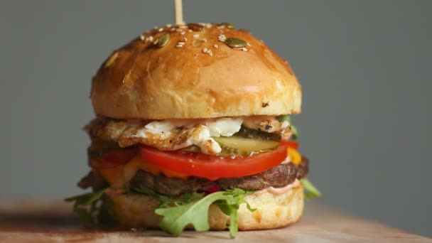 Gran hamburguesa con chuleta de res, tomates, champiñones y pepinos con queso derretido gira sobre un tablero de madera sobre fondo claro . — Vídeos de Stock