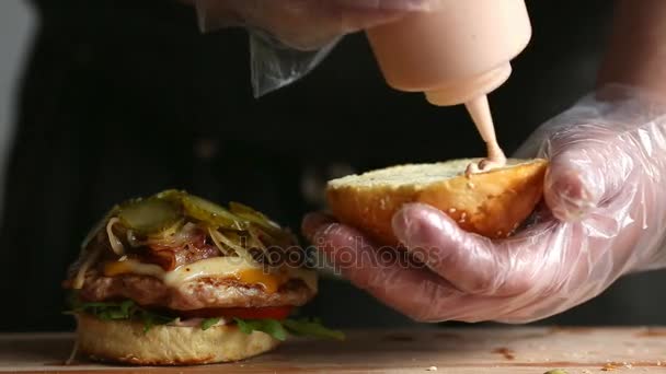 Η διαδικασία του μαγειρέματος μεγάλο Burger είναι επαγγελματίας σεφ, γκρο πλαν. Αλείψτε το κουλούρι με τη σάλτσα και να συγκεντρώσει το Burger — Αρχείο Βίντεο