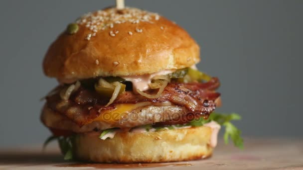 쇠고기 돈 까 스, 토마토, 버섯, 녹 인된 치즈와 오이 훌륭한 햄버거 밝은 배경에 나무 보드 회전. — 비디오