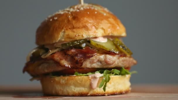 Μεγάλο Burger με μπιφτέκι μοσχάρι, ντομάτες, μανιτάρια και αγγούρια με λιωμένο τυρί περιστρέφεται σε έναν ξύλινο πίνακα επάνω ελαφρύς υπόβαθρο. — Αρχείο Βίντεο