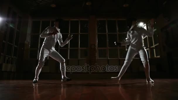 Joven hombre y mujer vestidos con disfraces para la práctica de esgrima en la sala de deportes. De vuelta al fondo está nevando. Movimiento dinámico horizontal de la cámara derecha e izquierda — Vídeos de Stock