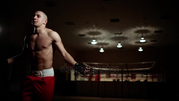Um homem bombeado de sapatos de boxe e shorts no ginásio contra o pano de fundo de um anel de boxe . — Vídeo de Stock