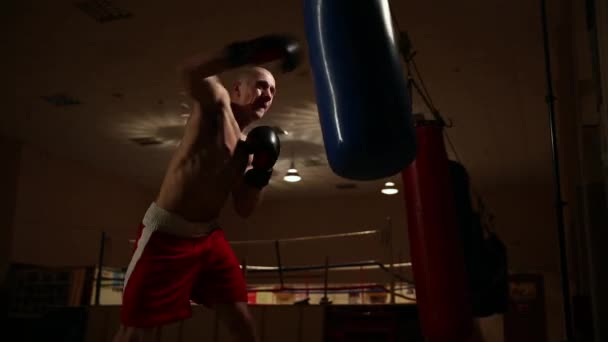 Um homem com roupas e luvas de boxe golpeia duramente a pêra. . — Vídeo de Stock