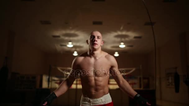 Een gepompt-up man in boksen schoenen en broek in de sportschool tegen de achtergrond van een boksring. Close-up — Stockvideo
