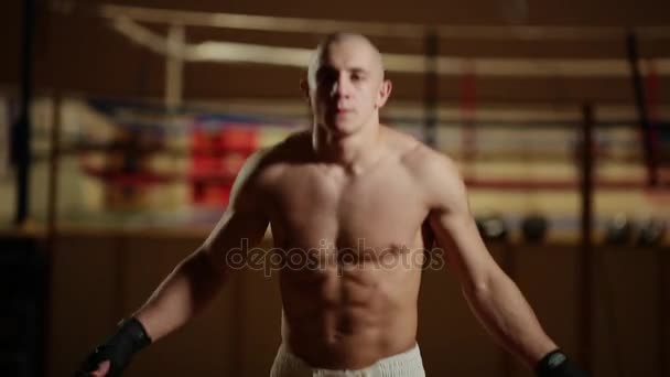 A pumped-up man in boxing shoes and shorts in the gym against the backdrop of a boxing ring. — Stock Video