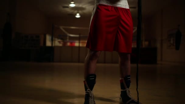 Een gepompt-up man in boksen laarzen en korte broek in de sportschool tegen de achtergrond van een boksring jurken pleisters op zijn handen. — Stockvideo