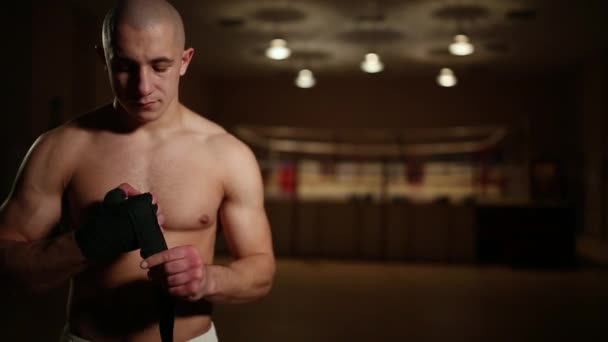 Un homme pompé dans des bottes de boxe et des shorts dans la salle de gym sur le fond d'un anneau de boxe robes bandages sur ses mains . — Video