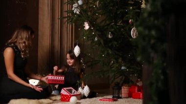 Yeni yıl hediyeleri Noel ağacının altında toplama bir kız ve annesi