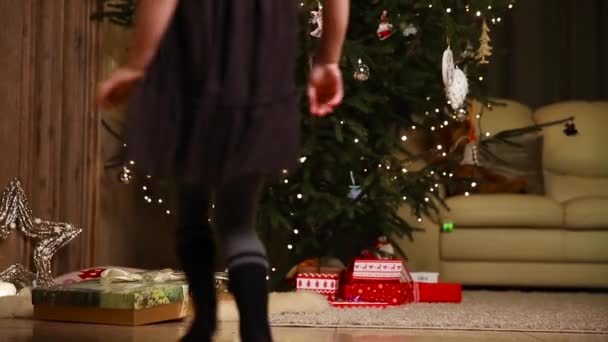 Een klein meisje wordt uitgevoerd om te openen een kerstcadeau onder de kerstboom. — Stockvideo