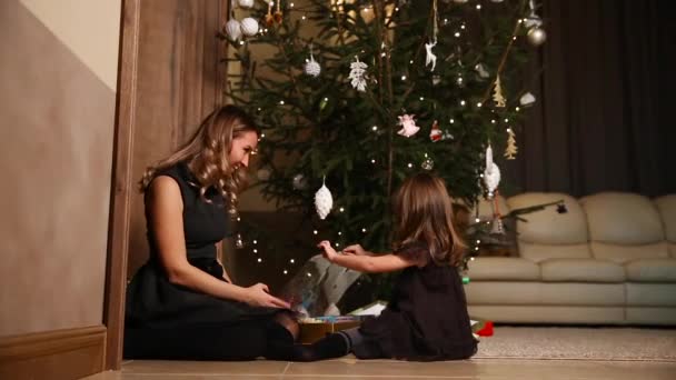 Maman et sa fille libèrent les rubans cadeaux de Noël sous le sapin dans le salon de leur maison — Video