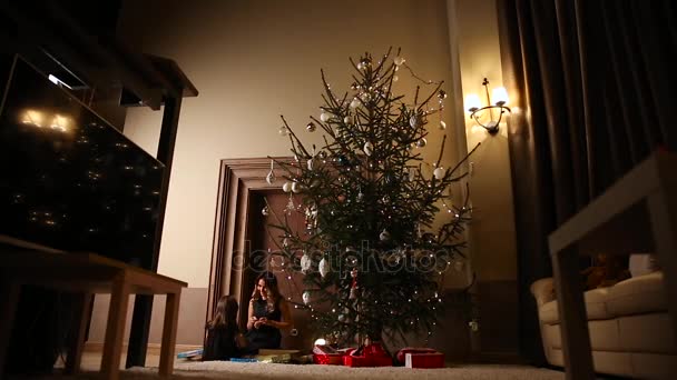 Μαμά και κόρη μαζί Ανοίξτε ένα χριστουγεννιάτικο δώρο κάτω από το δέντρο στο σαλόνι του σπιτιού τους. — Αρχείο Βίντεο