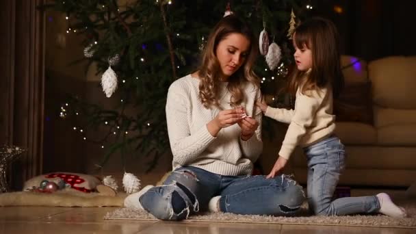 Mãe e a menina estão olhando para uma árvore de Natal sob uma árvore de Natal — Vídeo de Stock