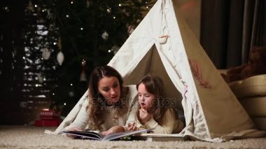 Beyaz kazak giyin, benim anne ve kızı bir peri masalı onunla yüklü bir ev çadırda yalan gece okumak için. Kız gülüyor ve anne gülümser