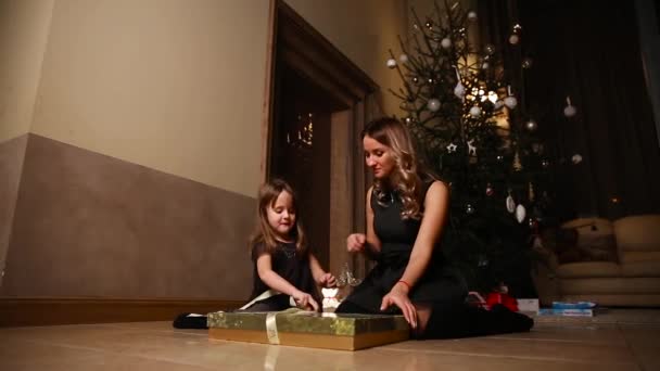 Mamá e hija sentadas bajo el árbol de Navidad regalos abiertos. La chica desatando la cinta del regalo. Plan global — Vídeo de stock