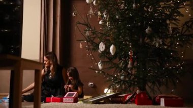 Anne ve kızı salmak Noel hediye şeritler evlerinin oturma odasında ağacının altında