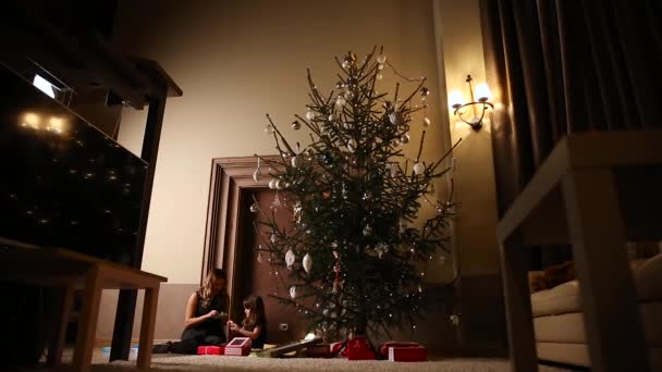 Mamá y su hija desatan las cintas de regalo de Navidad bajo el árbol en la sala de estar de su casa — Vídeo de stock