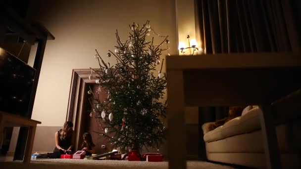 Мама и ее дочь выпускают рождественские ленточки под елку в гостиной своего дома — стоковое видео