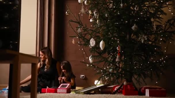 Mamma e sua figlia scatenano i nastri regalo di Natale sotto l'albero nel soggiorno della loro casa — Video Stock