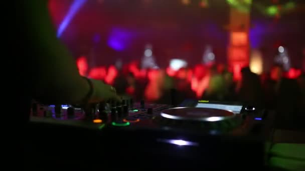 En primer plano es un mezclador de sonido para el trabajo de un DJ, y en el fondo de la espalda, la gente bailando . — Vídeos de Stock